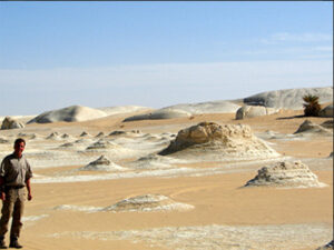 A lone tourist stands between sand and smaller limestone hills in the White Desert