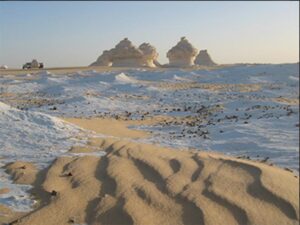 In the foreground, a rutted sand track leading through the White Desert towards various formations in the distance.