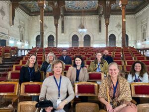 A group of tourists sit on red-cushioned chairs in the large illuminated plenary hall of the Cairo Tours: Geographical Society