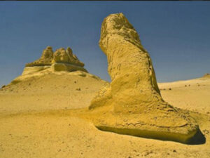 In the foreground a single rock, in the background a large collection of rocks in the desert