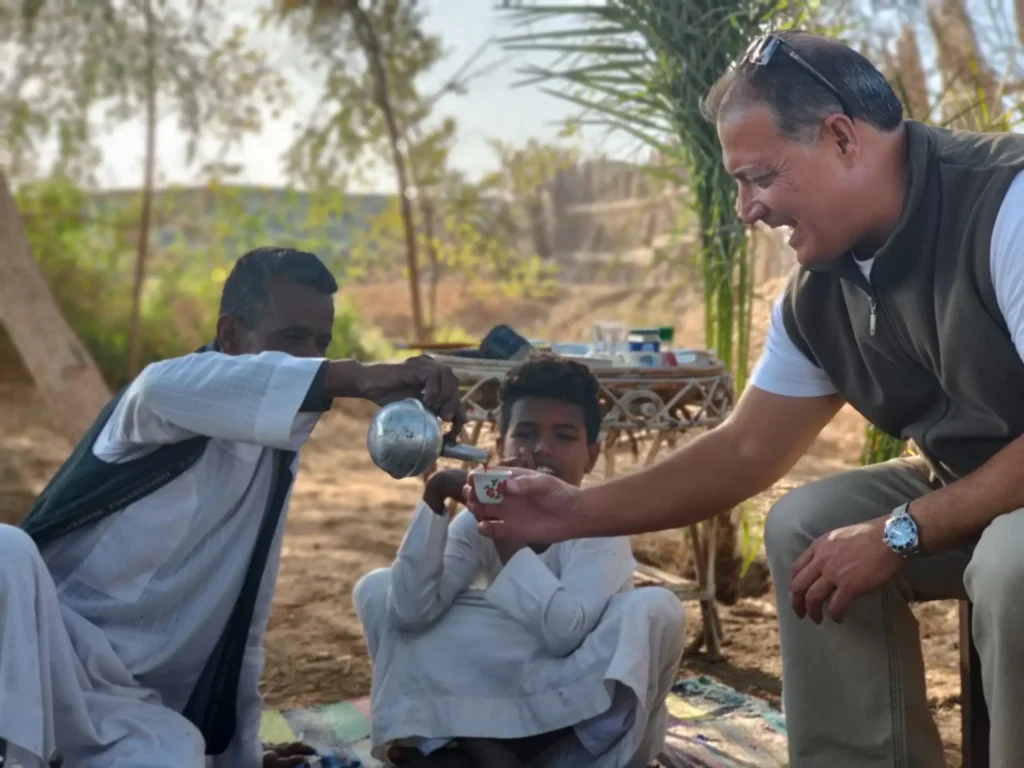 Tourist served in desert by two locals pouring drink from kettle