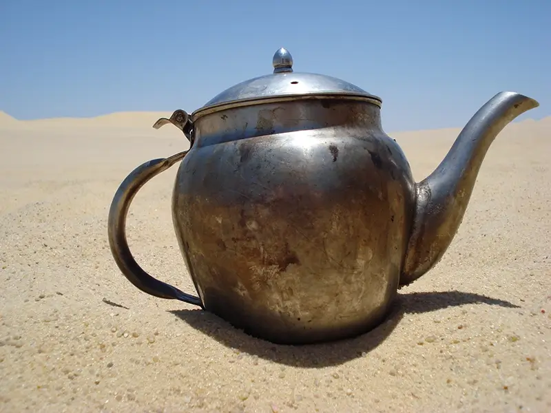 A silver slightly fire burnt teapot in the desert sand