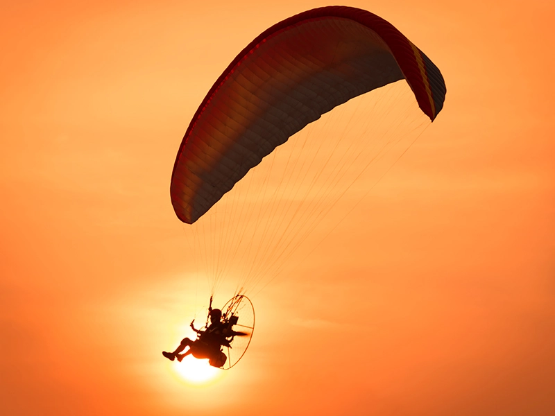 Paramotor silhouette in red orange sky with sun behind two paramotor gliders floating